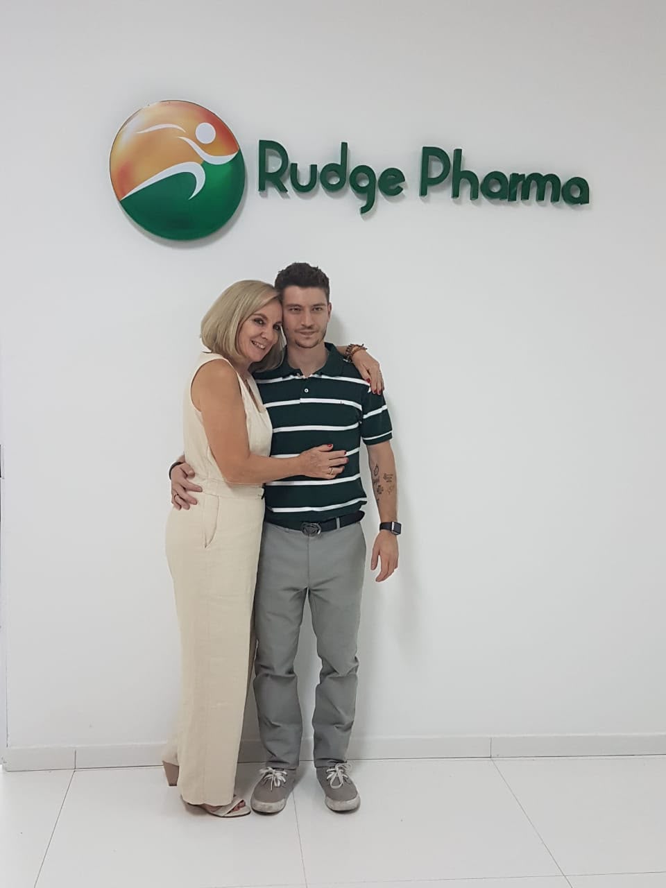 Equipe Rudge Pharma em frente ao logo da farmácia
